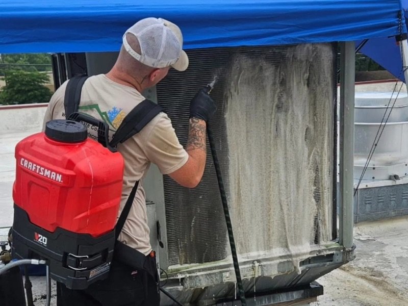 Technician cleaning a rooftop HVAC condenser coil during routine commercial maintenance