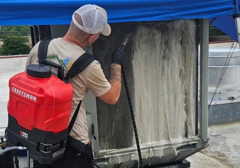 Technician cleaning a rooftop HVAC condenser coil during routine commercial maintenance